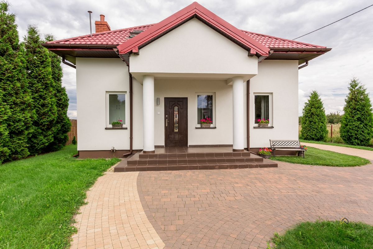 Tradycyjny dom jednorodzinny z czerwonym dachem, kolumnowym wejściem i zadbanym ogrodem